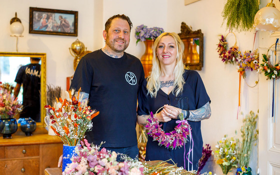 Zwei Personen stehen in einem Blumenladen zwischen Trockenblumen; eine h&auml;lt einen pinken Blumenkranz., Foto: Andreas Franke, Lizenz: Andreas Franke