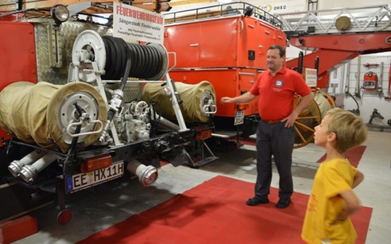 Ein Museumsf&uuml;hrer erkl&auml;rt einem Kind historische Feuerwehrfahrzeuge im Feuerwehrmuseum Finsterwalde, Foto: Pressestelle Finnstrwalde, Lizenz: Pressestelle Finsterwalde
