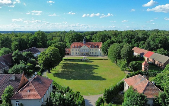 Luftaufnahme vom Schloss Grochwitz mit rotem Dach, gro&szlig;er Wiese, Nebengeb&auml;uden und dichtem Wald unter blauem Himmel., Foto: Bettina Unterkofler, Lizenz: Bettina Unterkofler